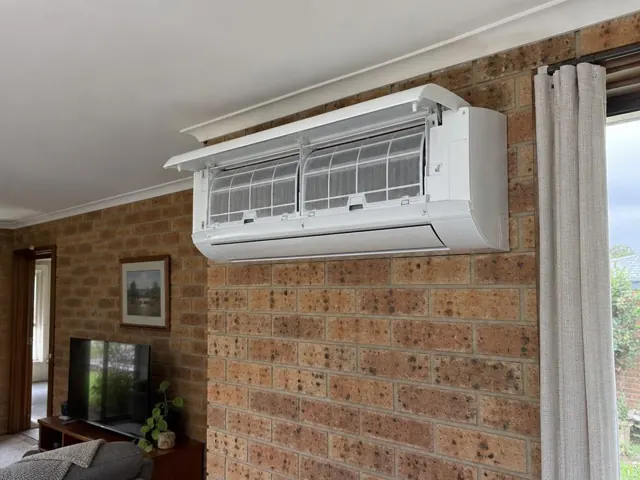 Clean split system with open front panel and visible filters on a brick wall living room in Wynn Vale