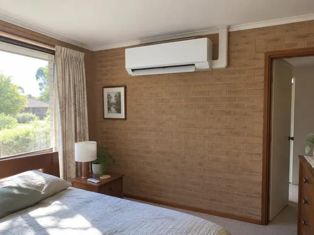 Indoor split system mounted high on a brick bedroom wall with louvre open in Greenwith