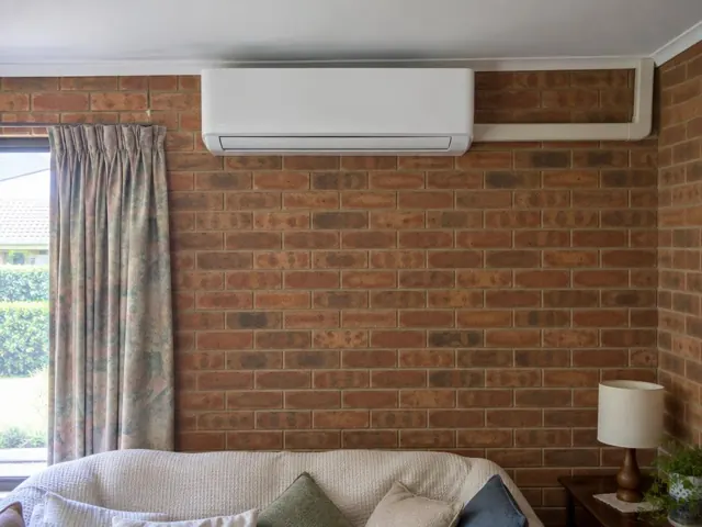 Wall-mounted split system above a brick feature wall and lounge in a living room in Wynn Vale